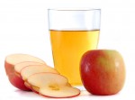 Slices apples laying beside a glass of apple cider vinegar