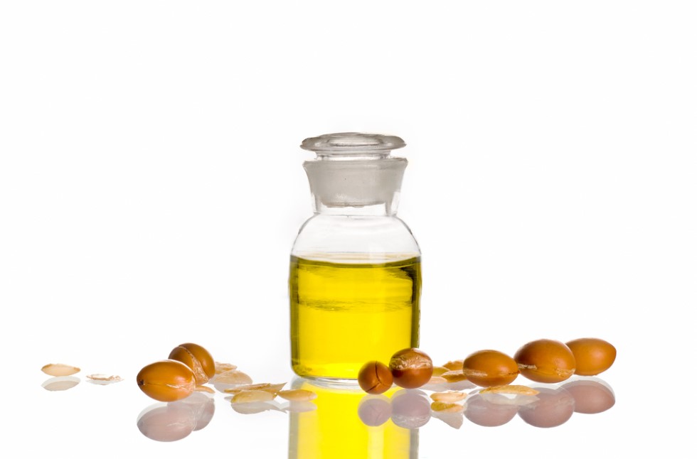 Bottle of Argan oil stands surrounded by Argan beans - shown to symbolize its potential use as a pure oil for topical use in seborrheic dermatitis