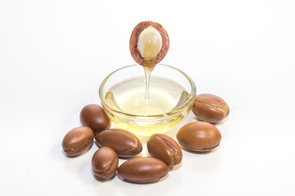 A partially peeled Argan bean hovering over a bowl of Argan oil - dripping a few drops of juicy oil directly into the bowl
